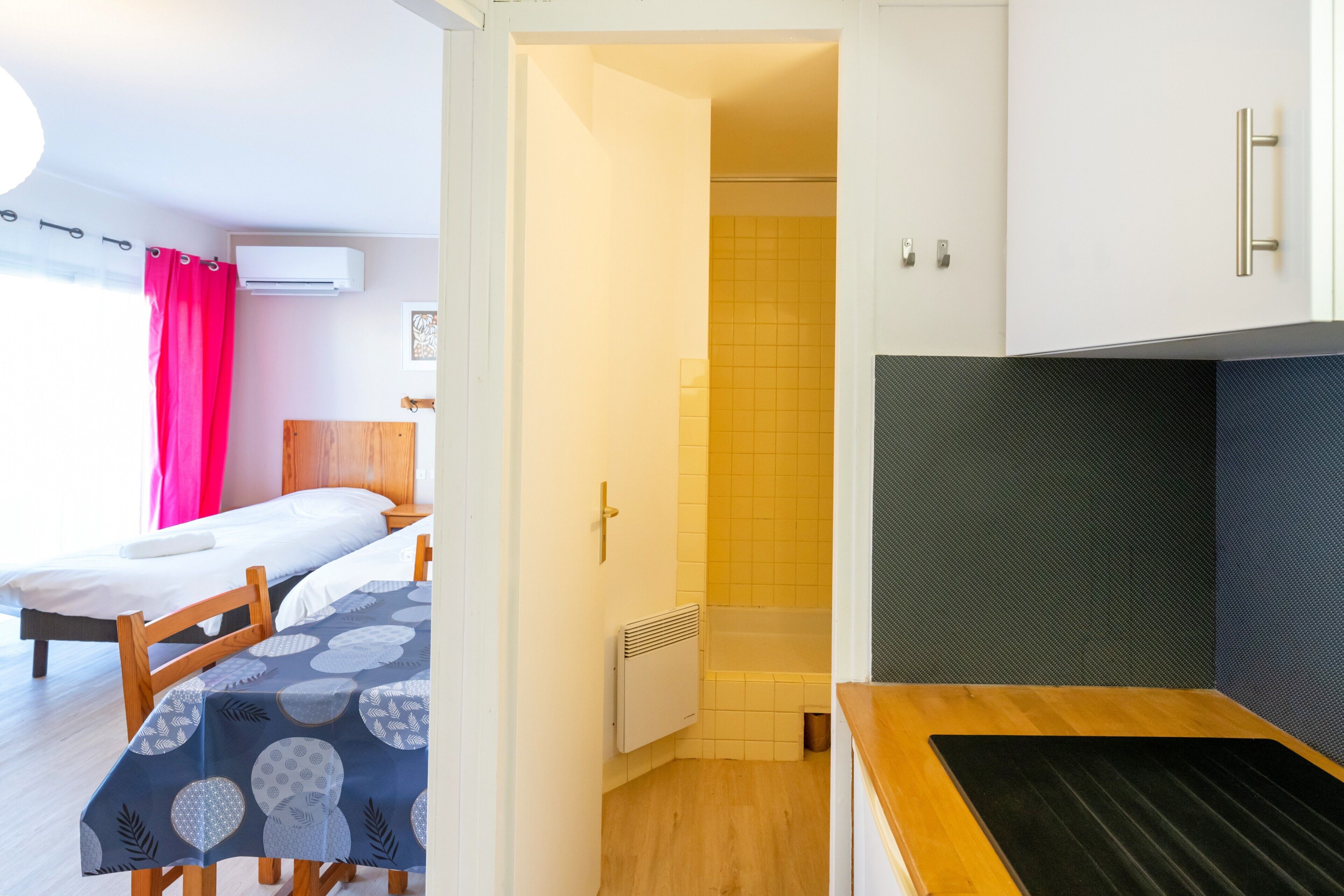 Ein Zimmer mit einem Bett, einem Tisch mit gemustertem Tischlein sowie einer Dusche und einem Heizkörper.