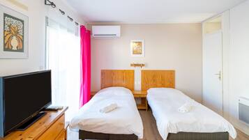 Une chambre d’hôtel avec deux lits simples, une télévision, une commode en bois, un appareil de climatisation et une fenêtre avec un rideau.