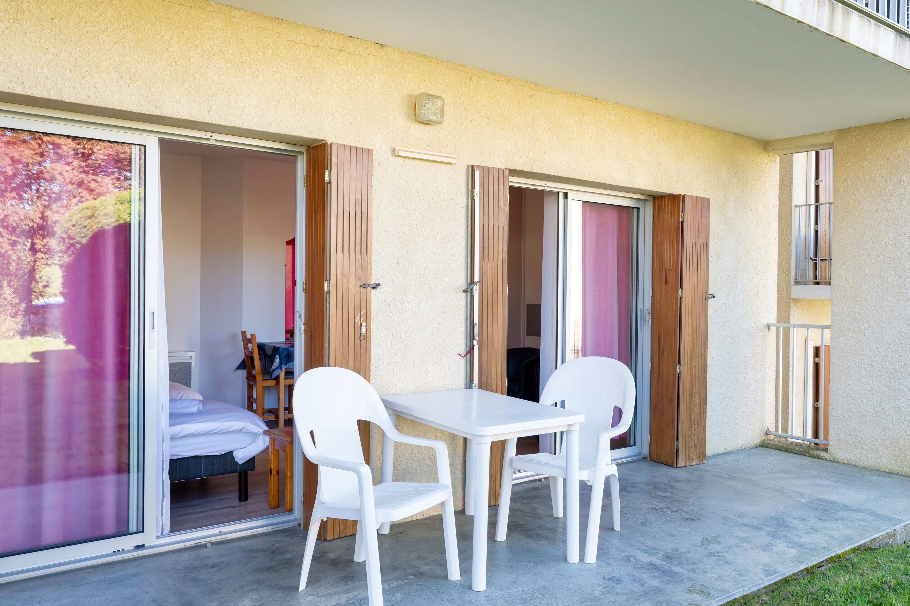 Un balcón con mesa y sillas, una puerta corrediza y una cama visible en el interior.