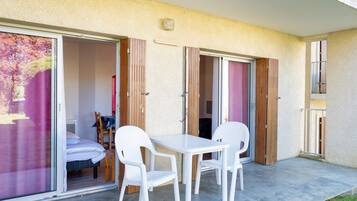 Un balcón con mesa y sillas, una puerta corrediza y una cama visible en el interior.