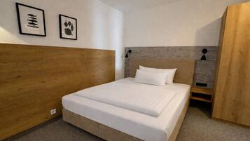A bedroom with a wooden headboard, a bed with white bedding, two framed pictures on the wall, and a small bedside table.