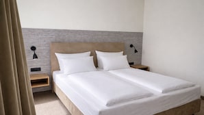 Een tweepersoonsbed met witte lakens, twee nachtkastjes met lampen, en een gestreepte muur achter het bed.