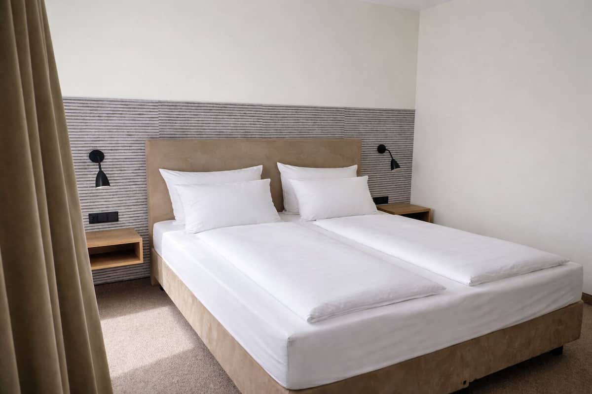 A double bed with white linens, two bedside tables with lamps, and a striped wall behind the bed.