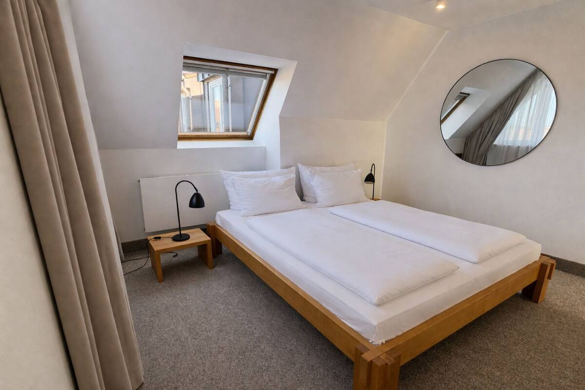 A bedroom with a skylight, a round mirror, a bedside table, and a bed.