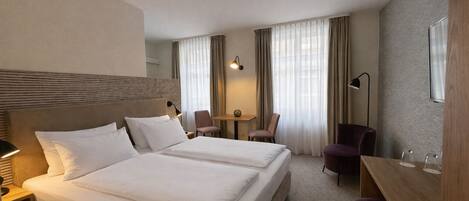 A hotel room with two beds, a desk, a chair, and a lamp.