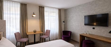 A hotel room with two beds, a desk, two chairs, a TV, and a lamp.