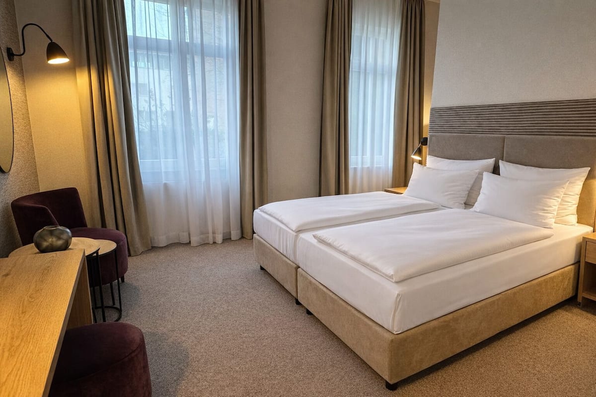 A hotel room with a double bed, a desk, a chair, and a lamp.