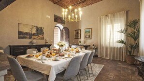 A dining room with a long table set for breakfast, a chandelier, and a large potted plant. - Villa Casale Belvedere by Interhome (Monsummano Terme)