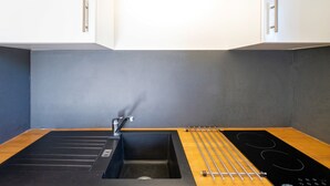 Una cocina moderna con un lavamanos negro, grifo de acero inoxidable y una placa de inducción negra.