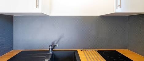 A modern kitchen with a black sink, stainless steel faucet, and a black induction cooktop.
