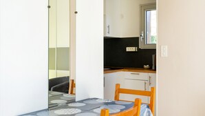 Una mesa de comedor con mantel estampado, sillas de madera, una zona de cocina con armarios y una ventana.