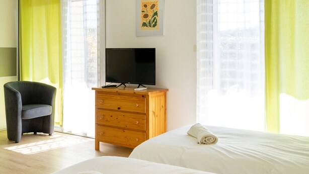 Habitación de hotel con dos camas, un televisor sobre una cómoda de madera, una silla y una ventana con cortinas.