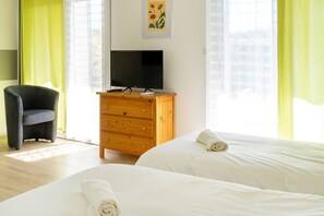 Habitación de hotel con dos camas, un televisor sobre una cómoda de madera, una silla y una ventana con cortinas.
