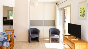 Una habitación con una mesa de comedor, dos sillas, un televisor sobre un mueble de madera y un armario con puerta corredera.