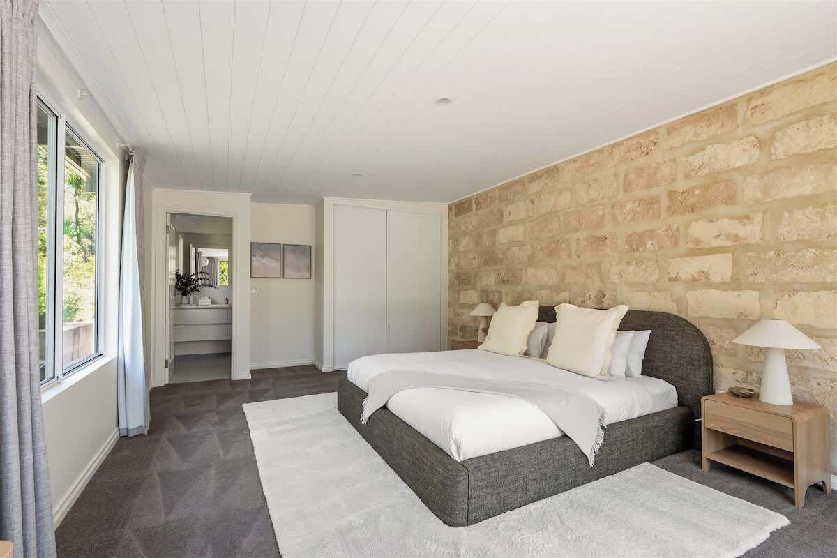A bedroom with a large bed, a nightstand, and a stone wall.