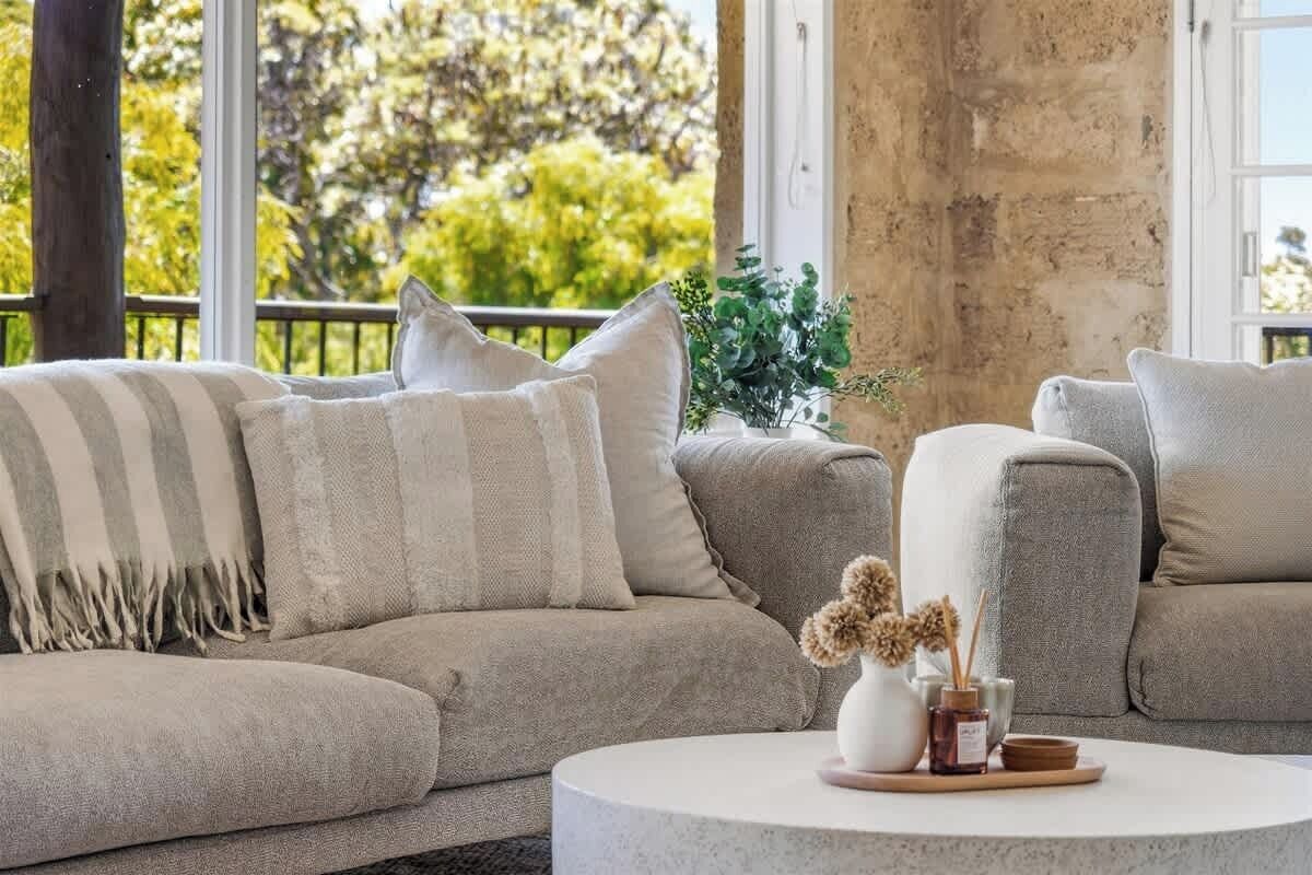 A living room with a sofa, a round coffee table, and a view of trees through large windows.