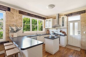 Een keuken met een groot eiland, witte keukenkastjes en uitzicht op groen.