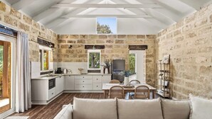 A modern kitchen with stone walls, a dining area with a table and chairs, and a cozy seating area with cushions.