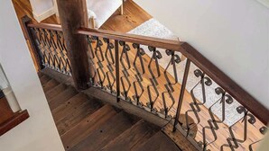 Un escalier en bois avec une rampe en métal, menant à une pièce dont un mur est blanc et qui possède une fenêtre.