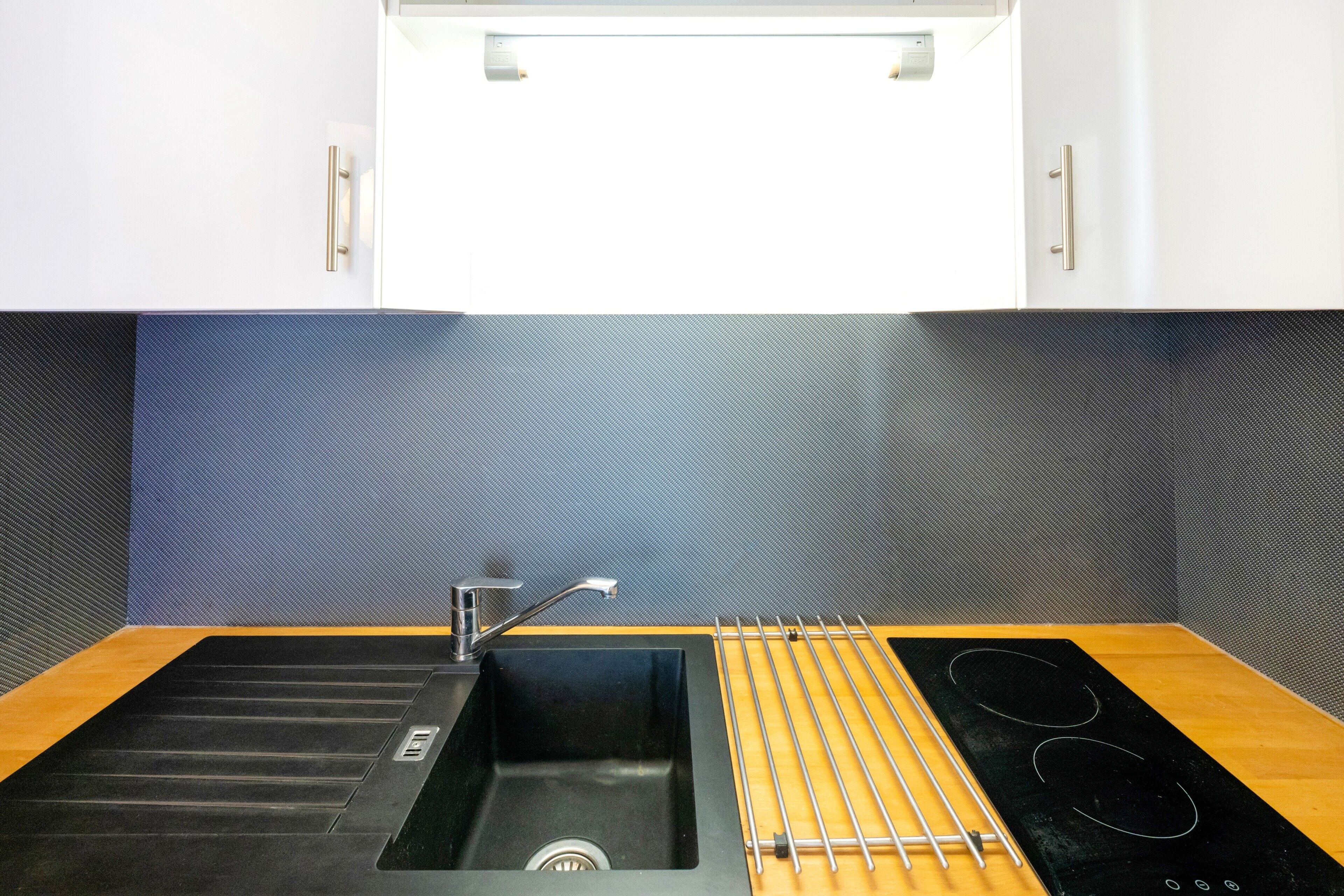 Une cuisine moderne dotée d’un évier noir, d’un robinet en acier inoxydable et d’une plaque de cuisson à induction noire.