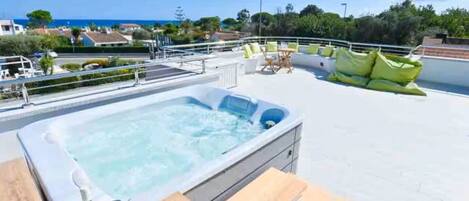 A rooftop pool with a hot tub, wooden deck, and outdoor seating.