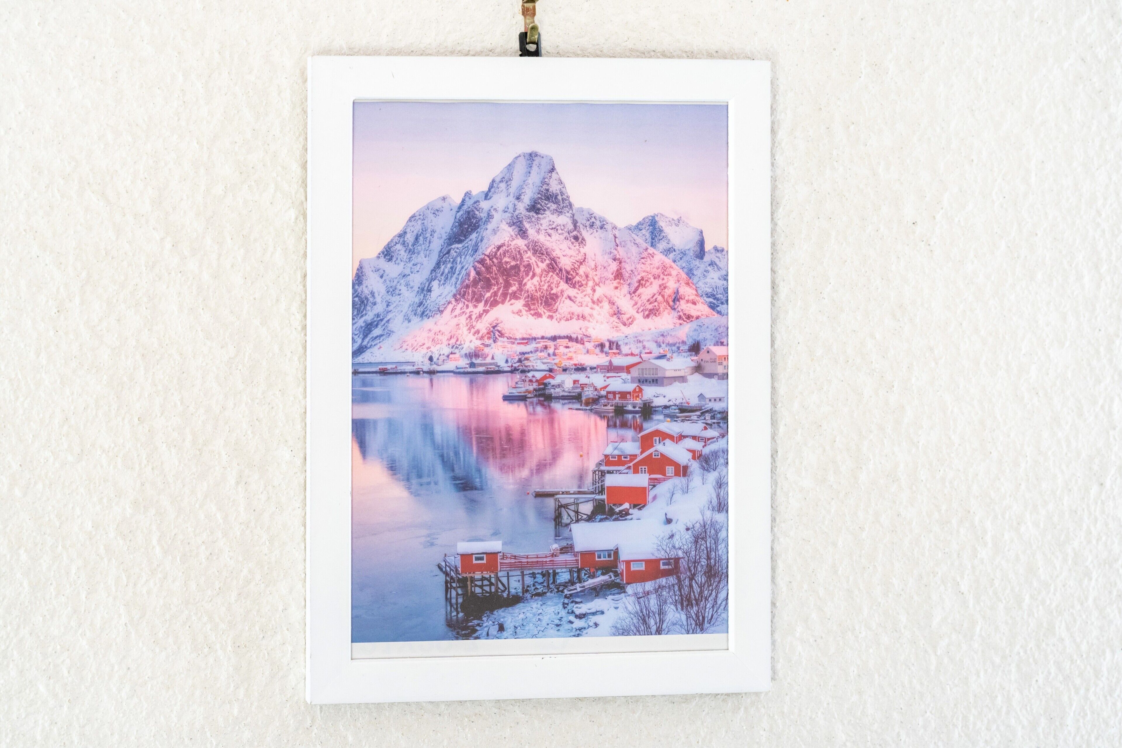 Une photographie encadrée représentant un paysage de montagne enneigé, avec un lac paisible et des bâtiments rouges.
