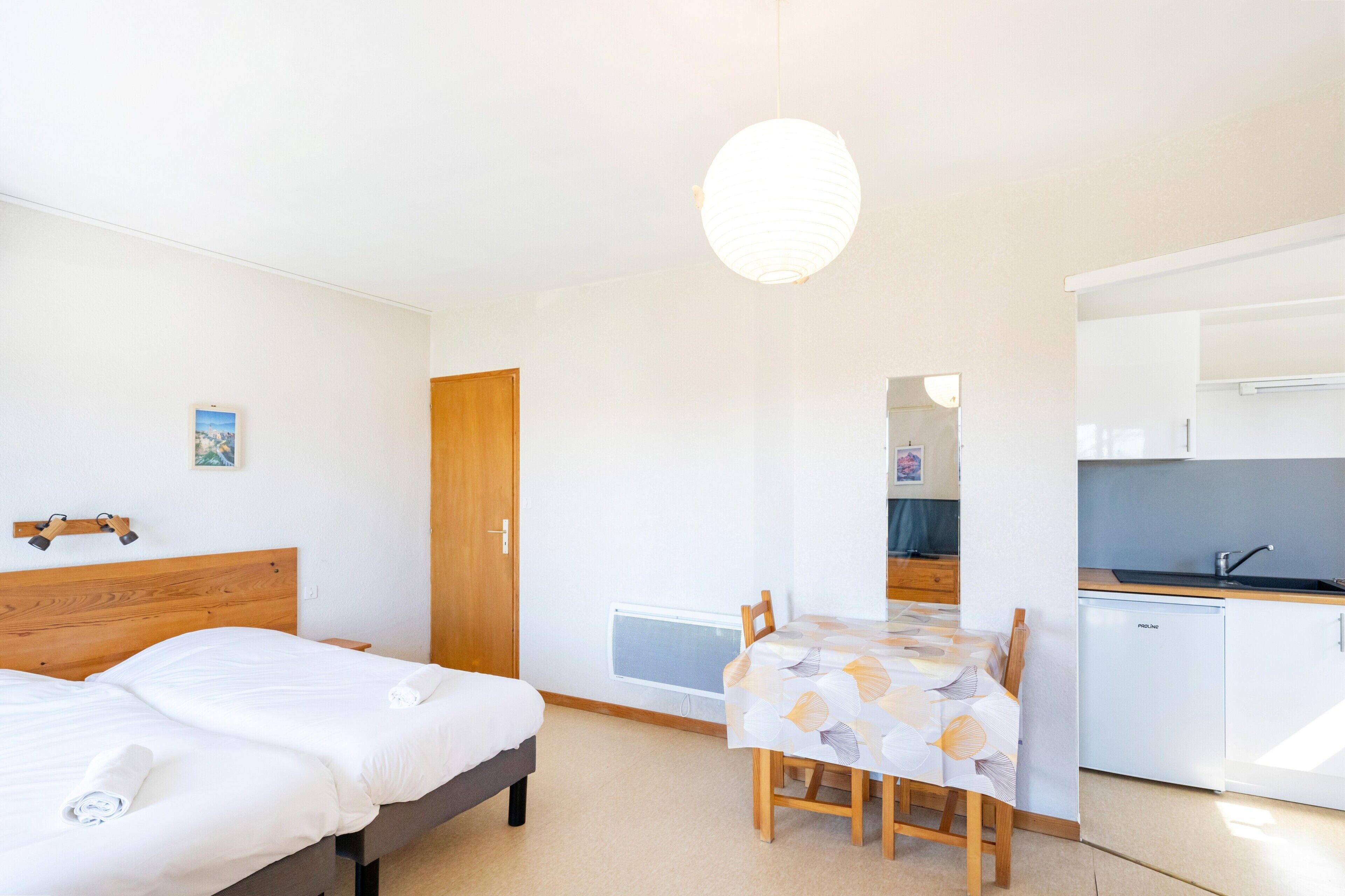 Een hotelkamer met twee bedden, een eettafel, een kitchenette en een groot raam.