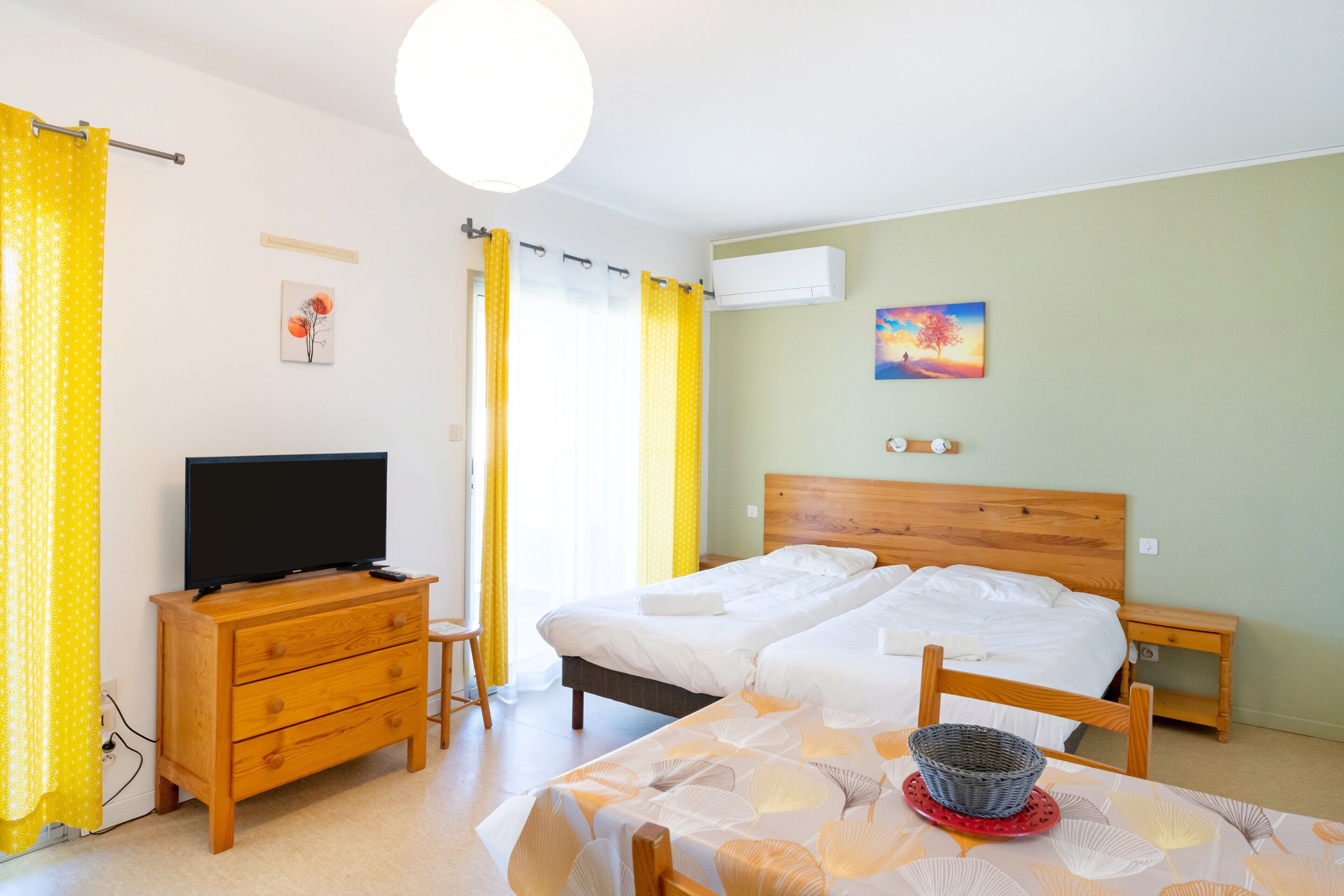 Quarto de hotel com cama, televisão, cómoda de madeira, mesa e um quadro na parede.