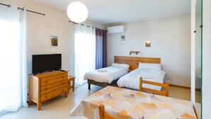 A hotel room with a bed, a TV, a wooden dresser, a table, and a ceiling light. - Cosy Studio with Balcony, Air Conditioning & Pool Table – Cazaubon (Cazaubon)