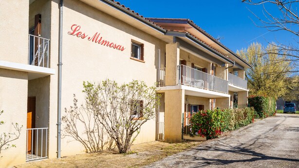 A building with a sign reading 'Les Mimosas,' balconies, and a clear sky. - Cosy Studio with Balcony, Air Conditioning & Pool Table – Cazaubon (Cazaubon)