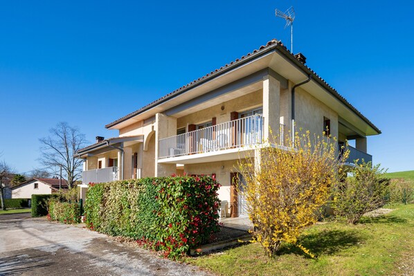 Ein zweistöckiges Haus mit Balkon, Garten und blauem Himmel.