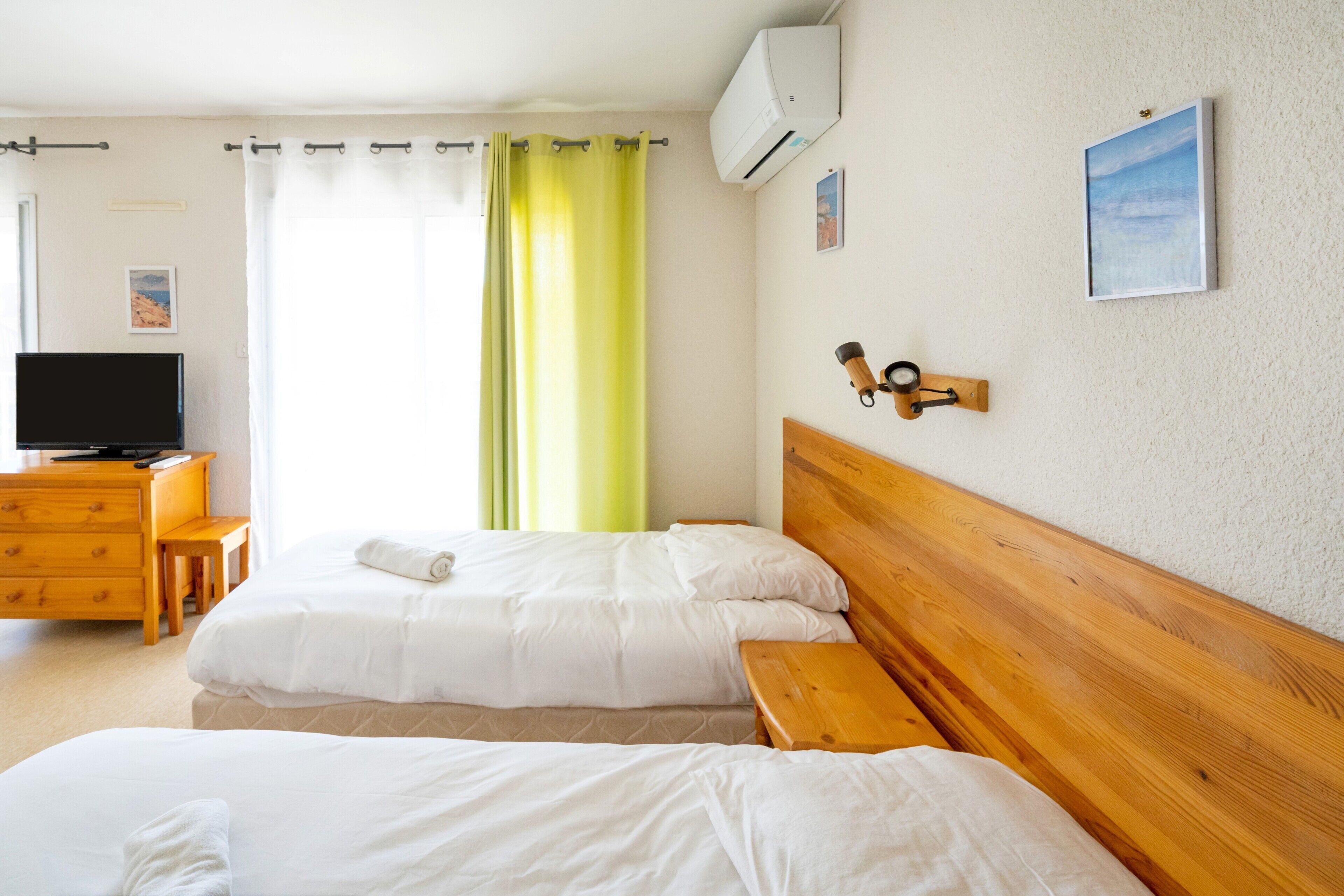 A hotel room with two beds, a wooden headboard, a television, a desk, and a window with curtains.