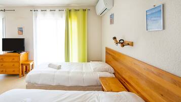 A hotel room with two beds, a wooden headboard, a television, a desk, and a window with curtains.