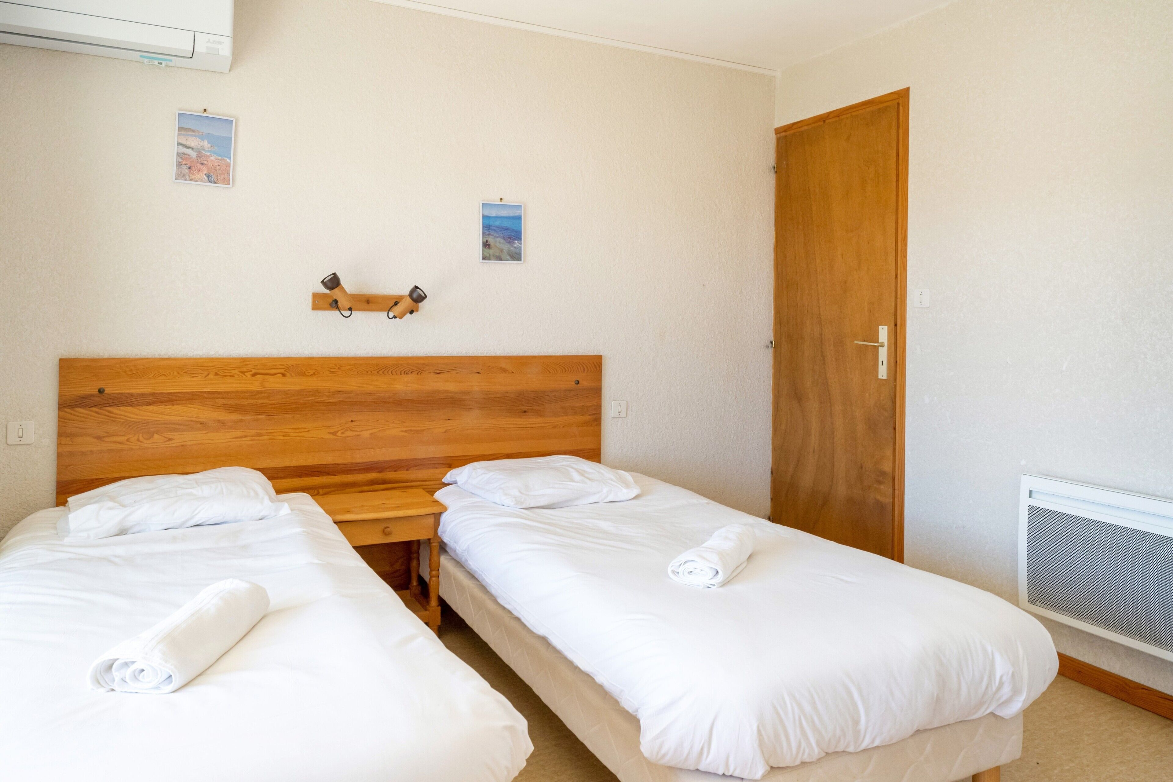 Une chambre avec deux lits simples, une tête de lit en bois, une petite table et une porte.