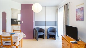 A room with a dining table, two chairs, a TV on a wooden dresser, and a sliding door. - Cosy Studio with Balcony, Air Conditioning & Pool Table – Cazaubon (Cazaubon)