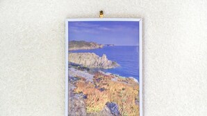 Pintura enmarcada de un paisaje costero sobre una pared con textura.
