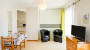 Una habitación con una mesa de comedor, dos sillas, un televisor sobre un aparador de madera y un armario con puerta corrediza.