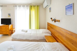 Habitación de hotel con dos camas, un cabecero de madera, un escritorio con una silla, un televisor y una ventana con cortinas.
