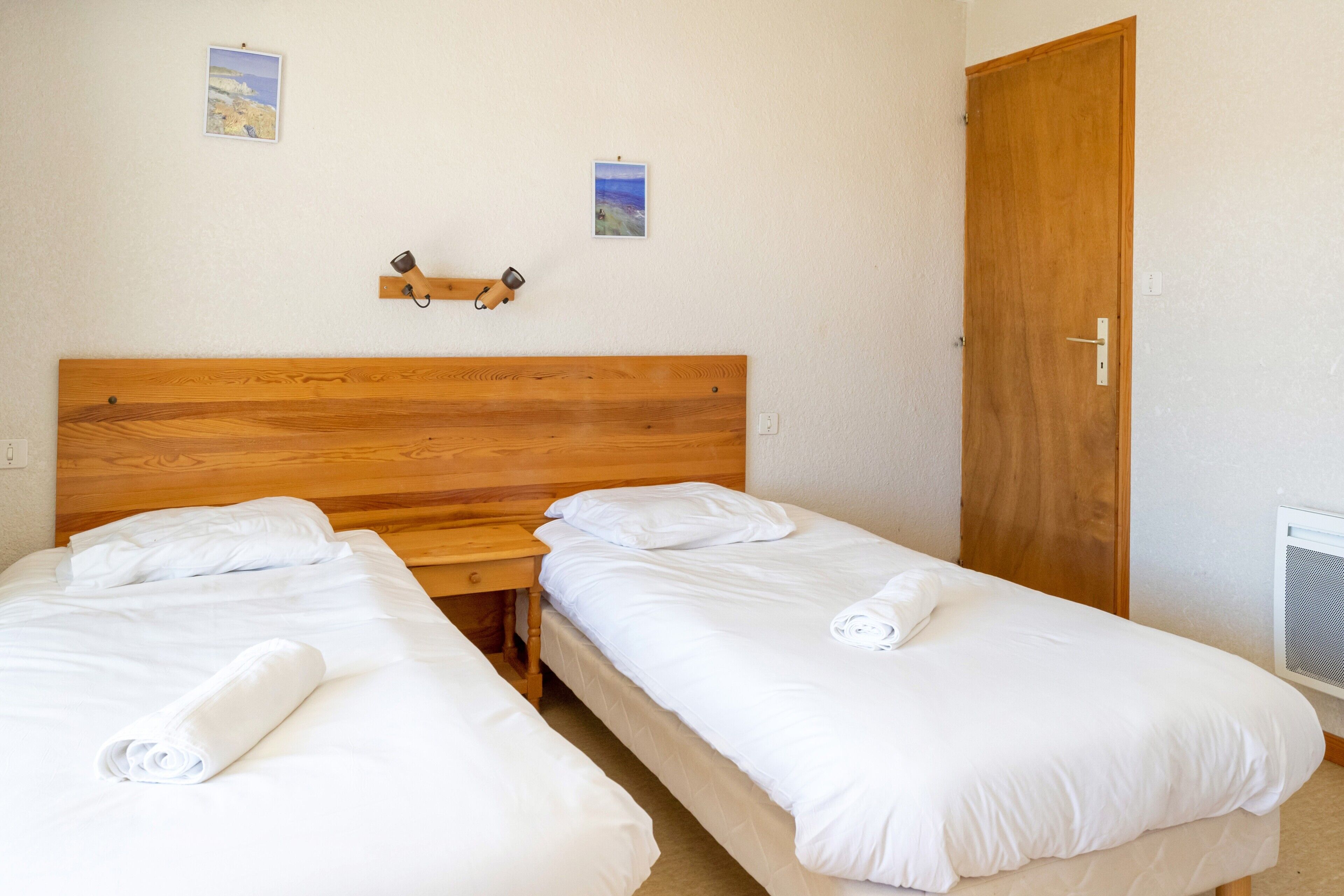 Ein Zimmer mit zwei Einzelbetten, einem Holzkopfende, einem Nachttisch und einer Tür.
