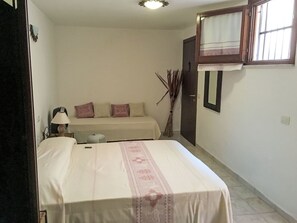 Ein kleines, sauberes Zimmer mit einem Bett, einem Nachttisch, einer Lampe, einem Fenster mit Vorhang und einer Tür.