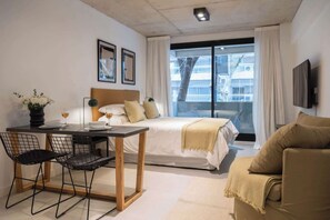 A hotel room with a bed, a dining table with chairs, a sofa, a TV, and a window with curtains. - Soho VIllage en Palermo by Magno | 101 (Buenos Aires)