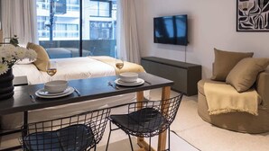 Una habitación de hotel con cama, una mesa de comedor con sillas, televisor en la pared y ventana con cortinas.
