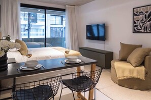 Ein Hotelzimmer mit Bett, Esstisch mit Stühlen, Fernseher an der Wand und einem Fenster mit Vorhängen.
