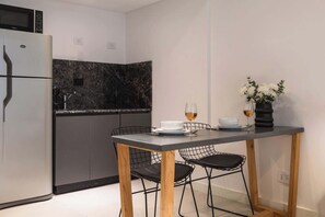A compact kitchen with a built-in microwave, a refrigerator, a marble backsplash, a dining table with chairs, and a vase with flowers. - Soho VIllage en Palermo by Magno | 101 (Buenos Aires)