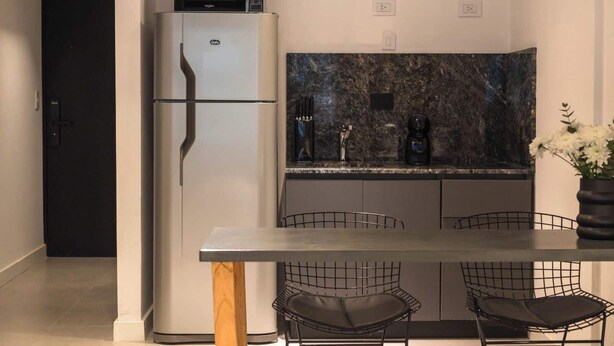 Una cocina moderna con microondas integrado, refrigerador, salpicadero de mármol, cafetera y comedor con mesa y sillas.