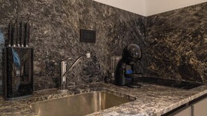 Una cocina con encimera de granito, pileta de acero inoxidable y cafetera.