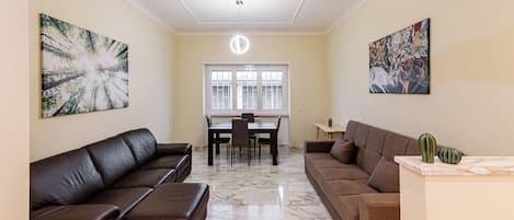A living room with two brown sofas, a dining table with chairs, and a ceiling light.