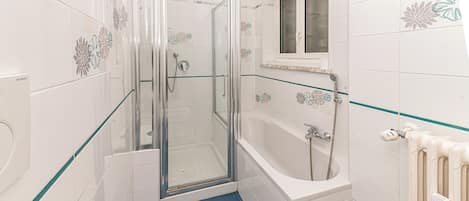 Ein Badezimmer mit einer gläsernen Duschkabine, einer Badewanne und einem Fenster über der Badewanne.