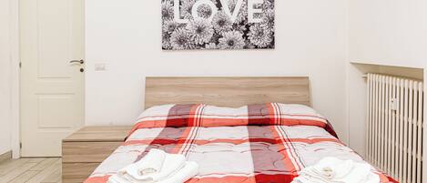 A neatly made bed with a red and white striped blanket, a wooden headboard, and a wall-mounted picture of flowers with the word "LOVE".
