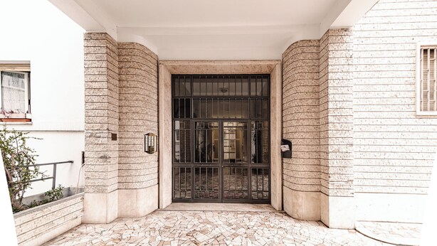 A building entrance with a tiled floor and a large metal gate. - Luca Flat - Tiburtina Train Station (Rome)